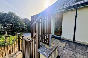 A wooden staircase leading to a covered outdoor area with a view of a garden and trees.