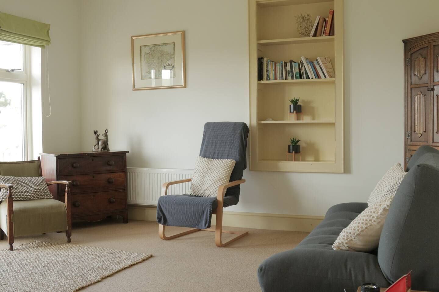 A living room with a sofa, a chair, a wooden dresser, a bookshelf, and a framed picture on the wall.