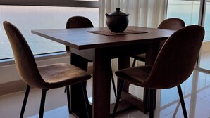 Una mesa de comedor con cuatro sillas, una olla sobre la mesa, y vistas al mar a través de amplias ventanas.