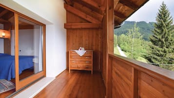 Un balcone in legno con un letto e una cassettiera, affacciato su una valle boscosa.