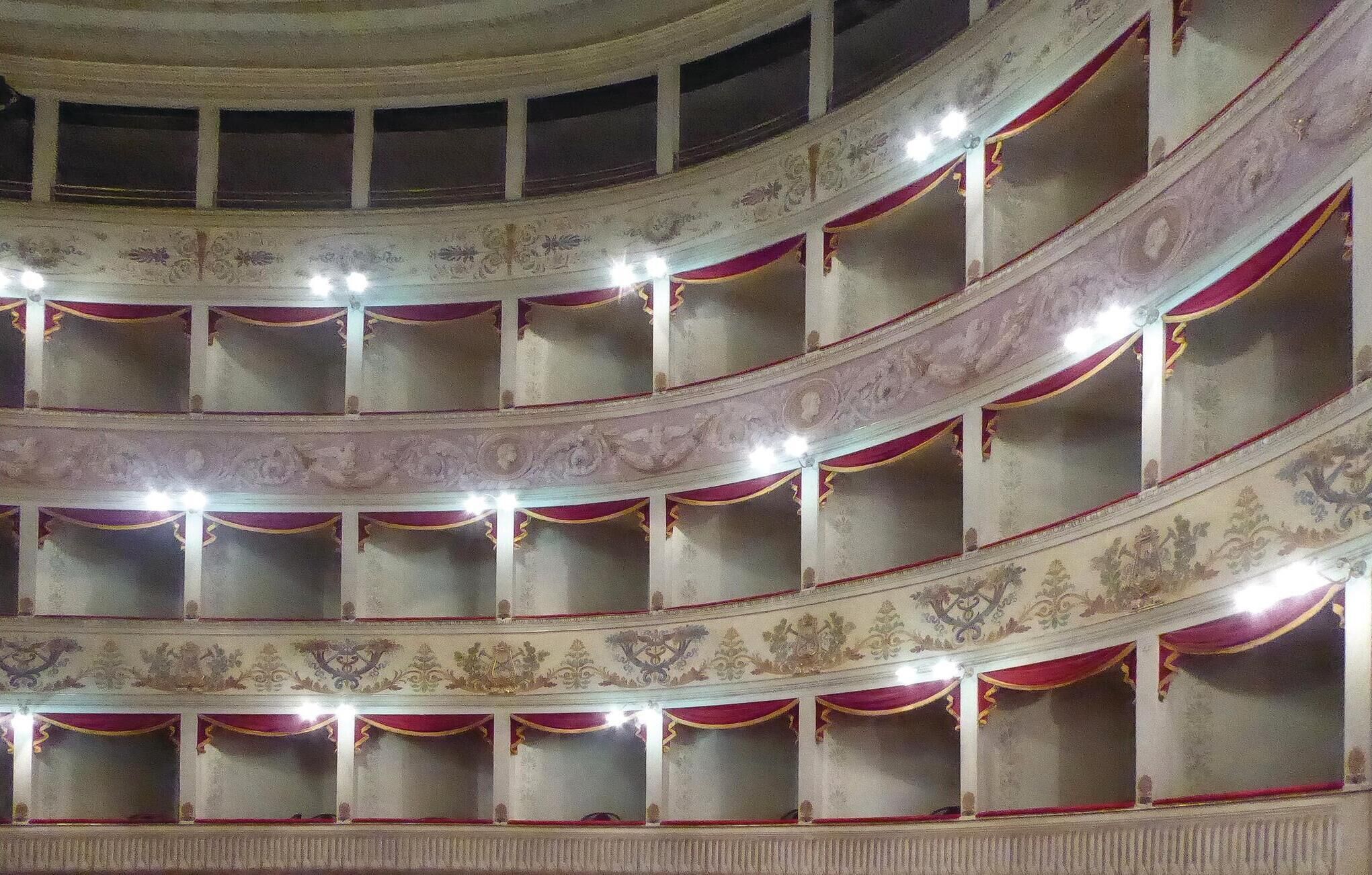 A multi-tiered auditorium with ornate wall decorations and red curtains.