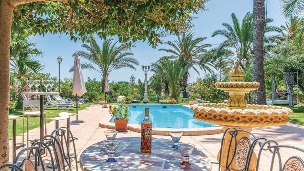 Ein Poolbereich mit einer Fontäne, Liegestühlen und einem Tisch mit Gläsern und einer Flasche.