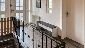 Een trap met een houten leuning en een zwarte metalen balustrade, die uitkomt op een plateau met een zwart-wit console tafel en een radiator.