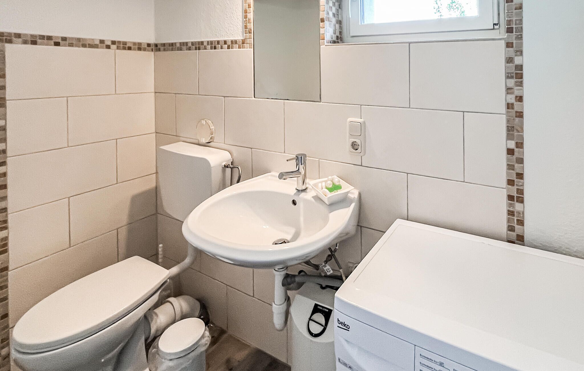Een kleine badkamer met toilet, wastafel en een raam boven de wastafel.