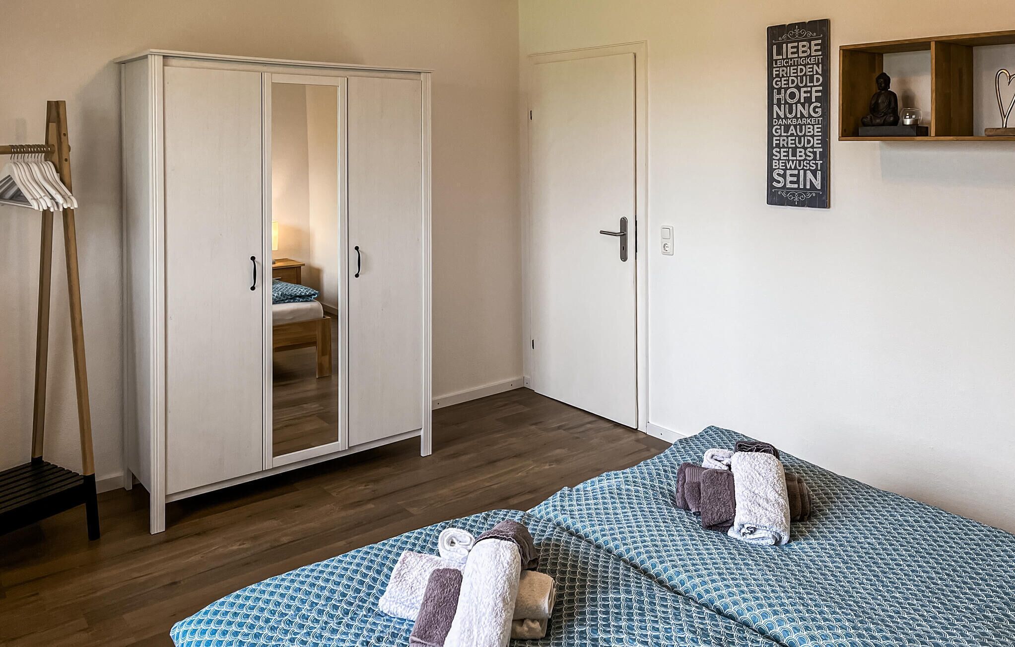 Une chambre avec une armoire, un lit avec une literie à motifs et un mur orné d’une citation inspirante.