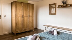 Een slaapkamer met een houten kledingkast, een bed met beddengoed met een patroon, een nachtkastje en een spiegel aan de muur.