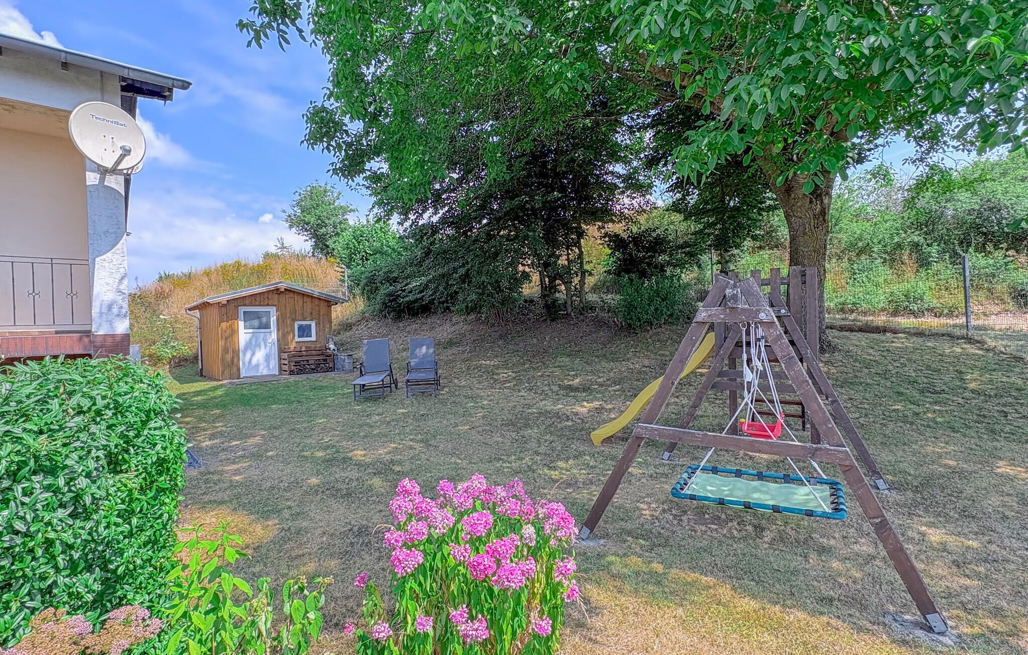 Un jardin avec une balançoire, un petit abri de jardin et une antenne parabolique.