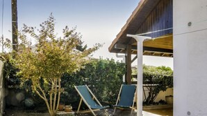 Un espacio al aire libre cubierto con dos sillones, un árbol pequeño y un edificio blanco.