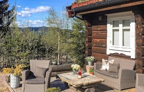 A log cabin with wicker furniture, a table with flowers, and a view of trees and mountains. - 4 bedroom beautiful home in Svarstad (Svarstad)
