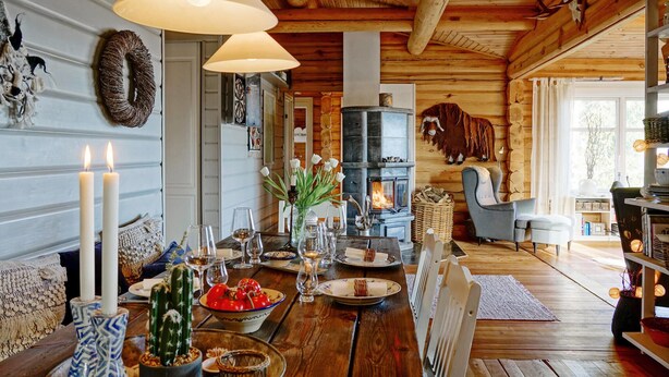 L’intérieur chaleureux d’un chalet, avec un décor en bois, une cheminée et un coin repas préparé pour un repas.