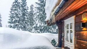Une cabane en bois, dont le toit est recouvert de neige, et qui possède une fenêtre à cadre blanc.