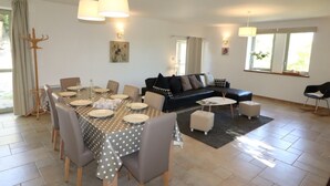 A dining area with a table set for six, a black sofa, and a coffee table in a bright living room with large windows. - Gite La Borie Haven of peace in the Perigord (Cénac-et-Saint-Julien)