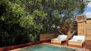 Een houten terras met een jacuzzi, twee ligstoelen en een hangmat.