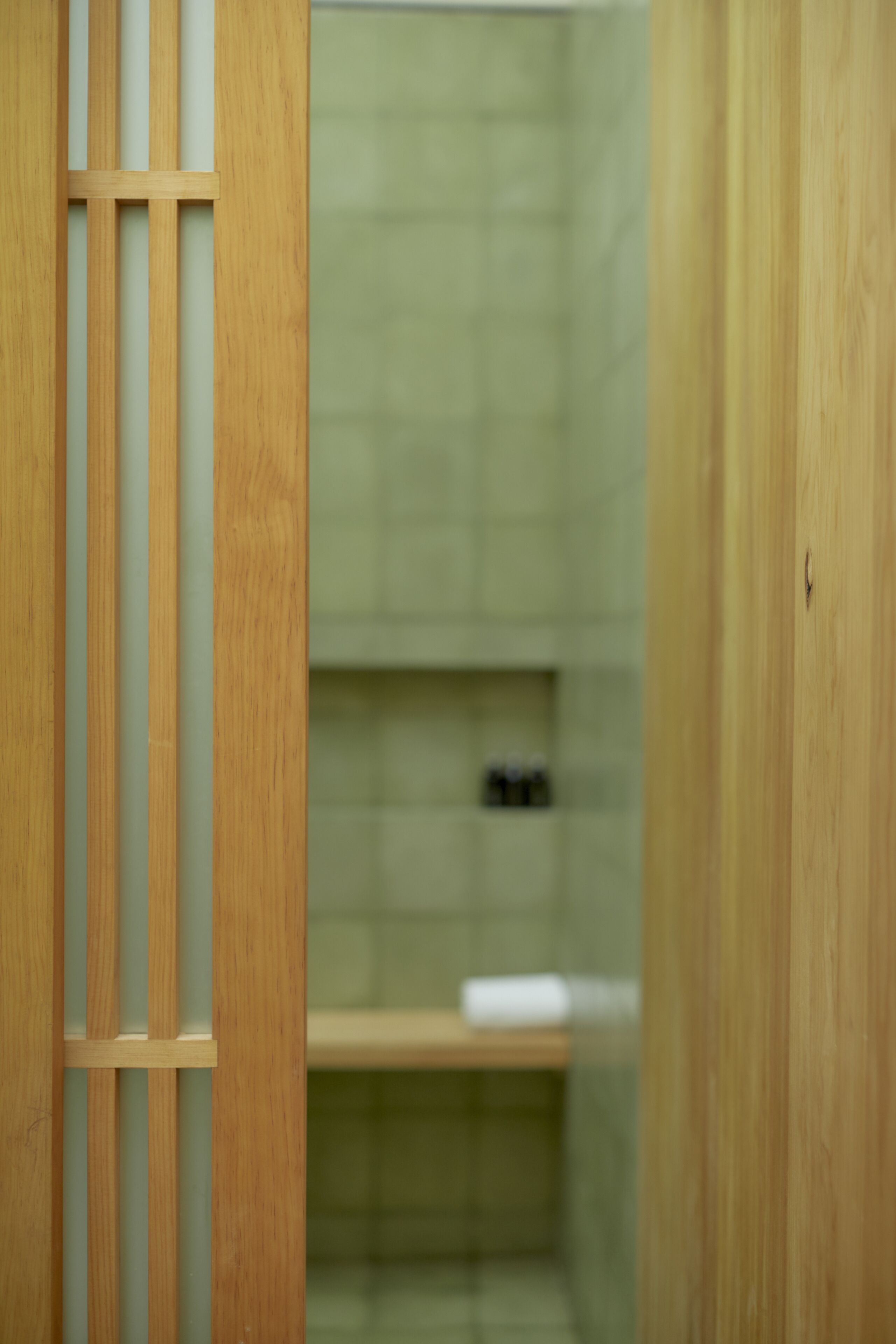 A wooden partition with vertical slats in a room with a tiled wall and a shelf with items on it.