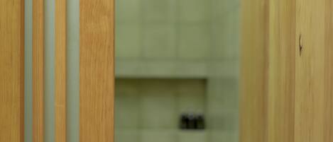 A wooden partition with vertical slats in a room with a tiled wall and a shelf with items on it.