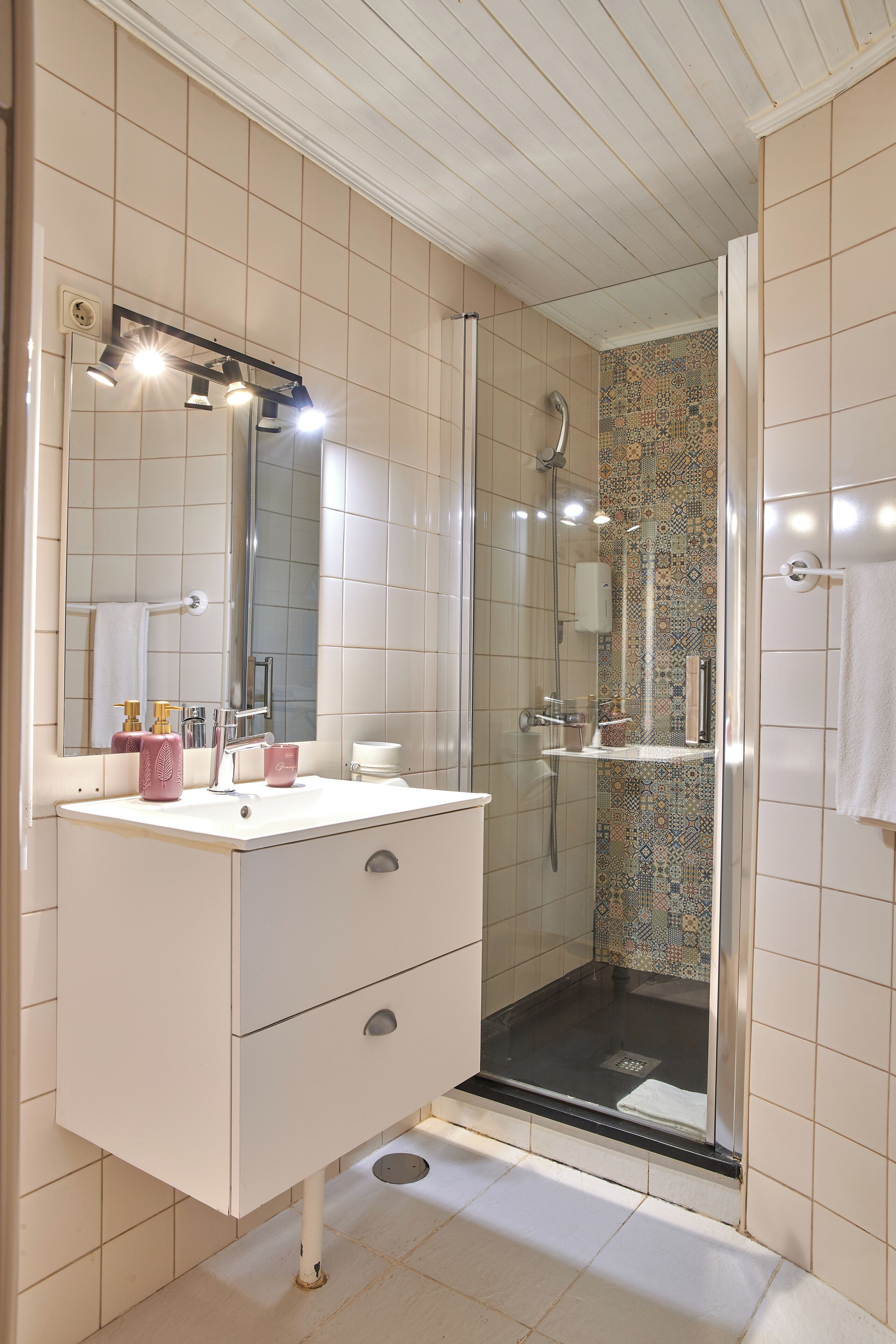 Un baño con tocador blanco, un espejo grande, cabina de ducha y suelo de baldosas.