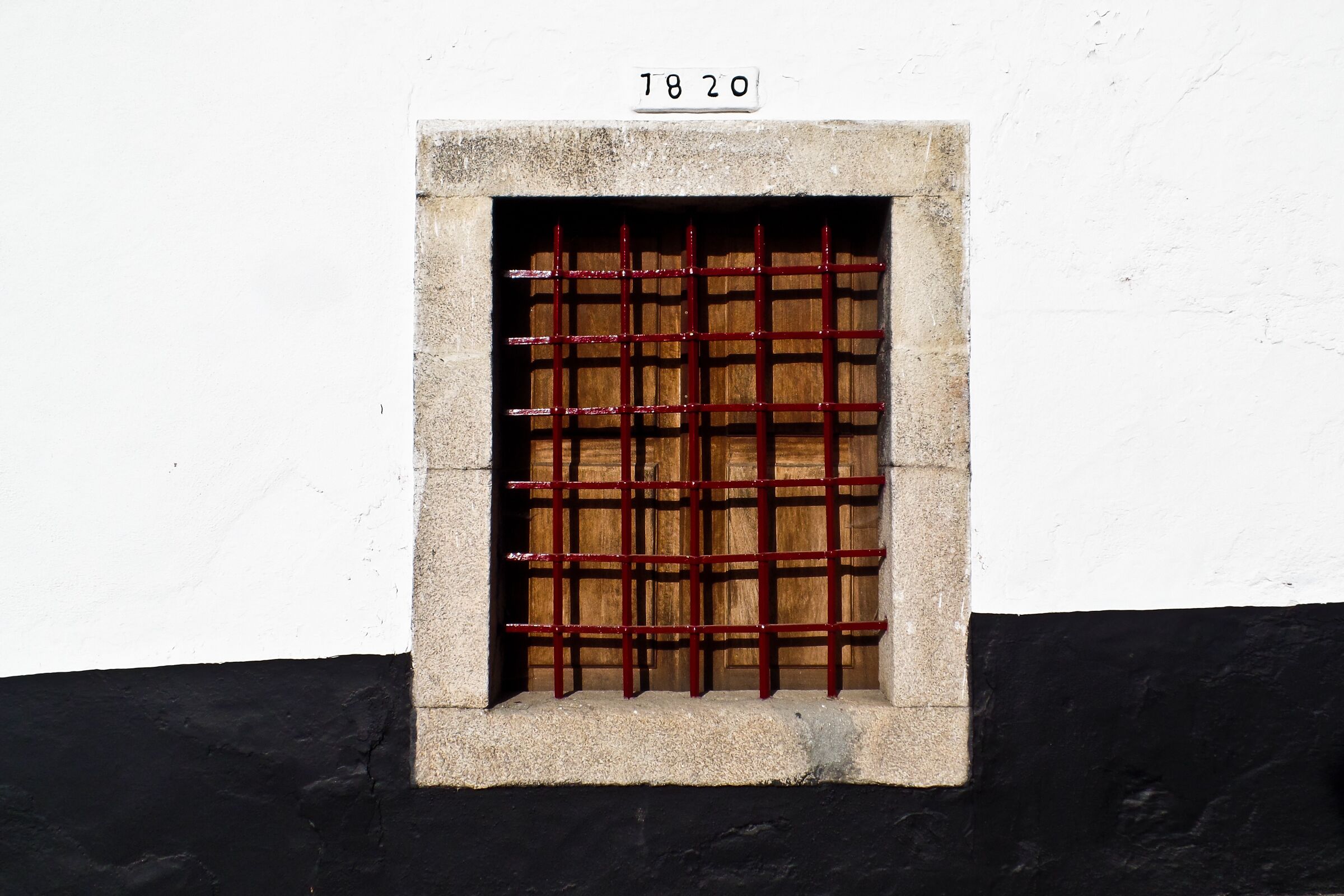 A window with a metal grid, a number '1820' above it, and a black and white wall.