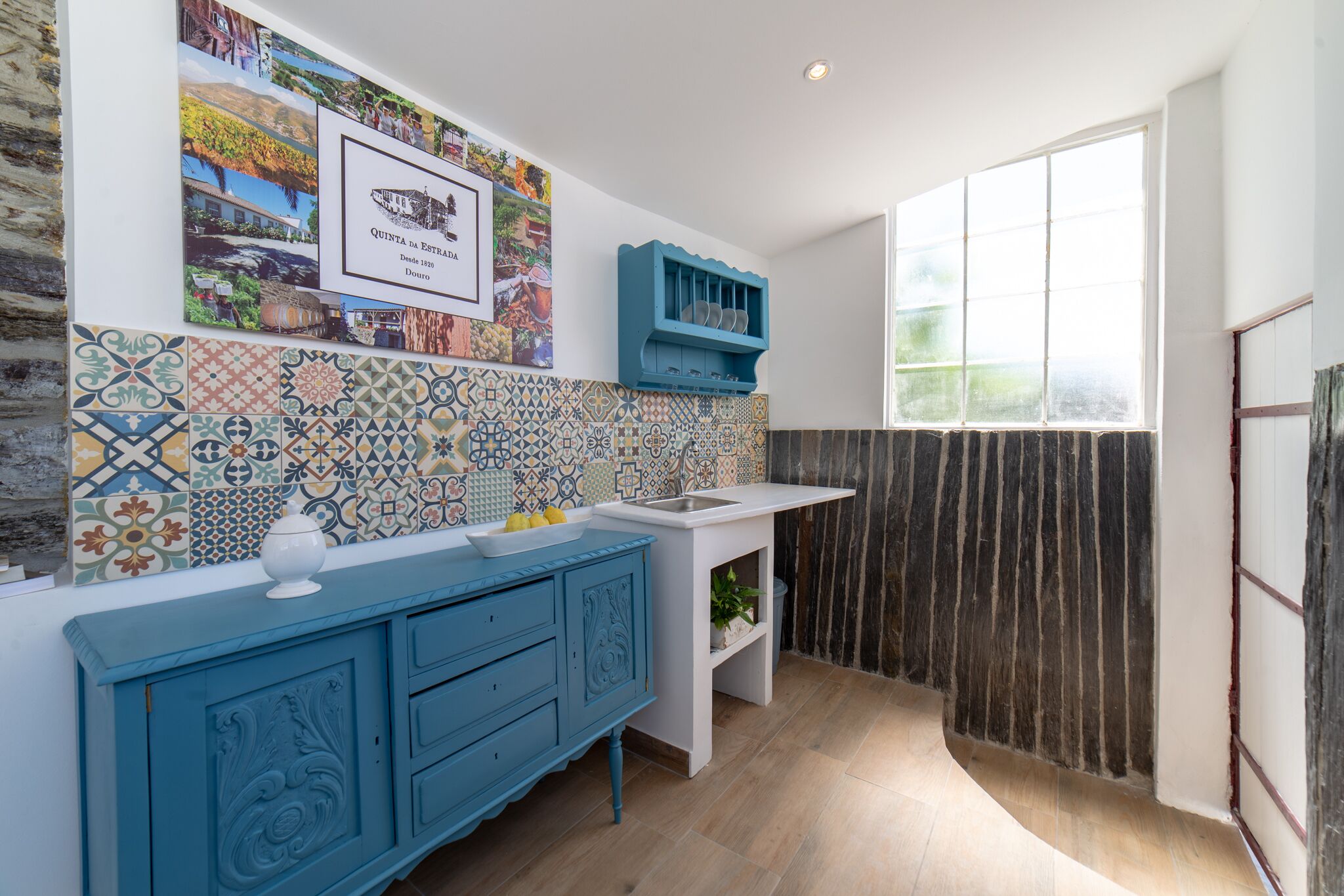 A kitchen with a tiled backsplash, a blue cabinet, a white countertop, and a window.