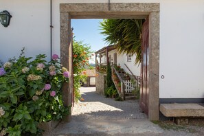 A cobblestone path leading to a building with a stone archway, a wooden fence, and potted plants.