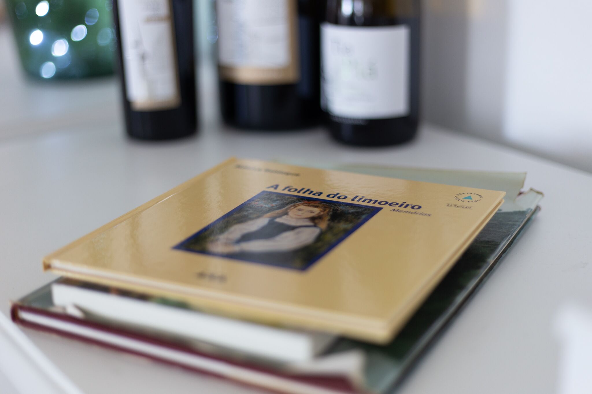 Un livre intitulé « A folha do limãoiro » est posé sur une table, avec un arrière-plan flou composé de bouteilles.