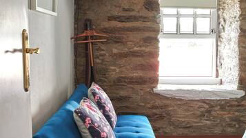 A room with a blue sofa, a wooden door, a stone wall, a window, and a television mounted on the wall.