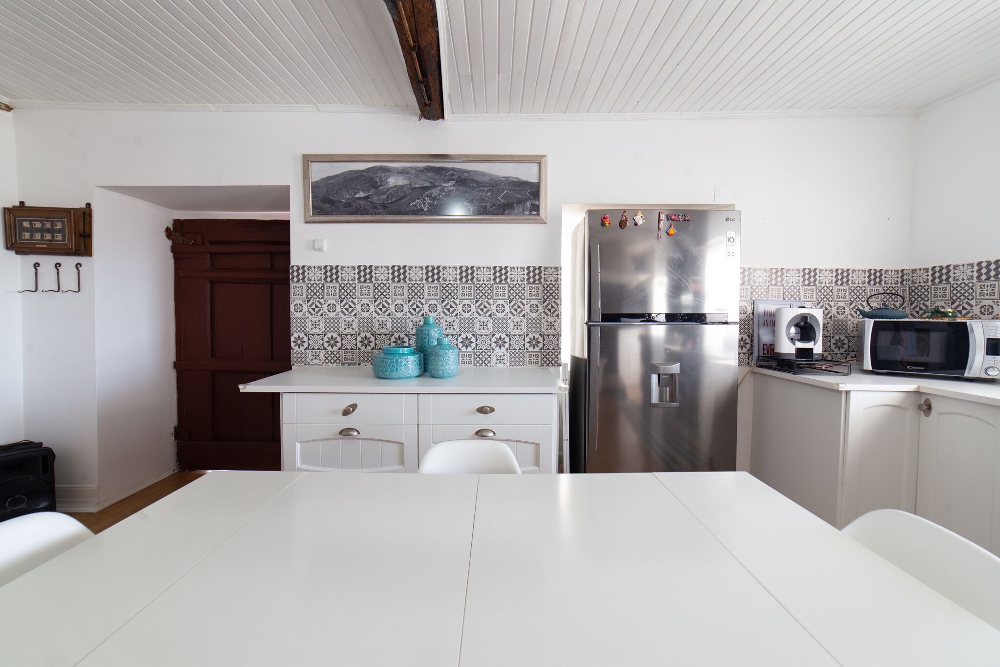 A kitchen with white cabinetry, a stainless steel refrigerator, a microwave, and a dining table.