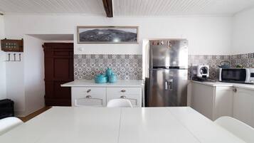 Una cocina con armarios blancos, un refrigerador de acero inoxidable, un microondas y una mesa de comedor.