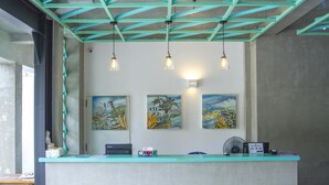 A reception desk with teal accents, three wall-mounted paintings, and a fan. - Somerset Mirissa Beach (Mirissa)