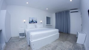 A modern hotel room with a large bed, a small bedside table, a wall-mounted artwork, a window with curtains, and an air conditioning unit. - Somerset Mirissa Beach (Mirissa)