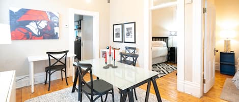 A modern living room with a dining area, featuring a white table, black chairs, and a contemporary chandelier.