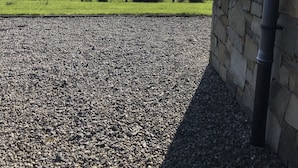 A view of a stone building with a gravel driveway and a wooden fence. - Mullach Cottage (Tourmakeady)