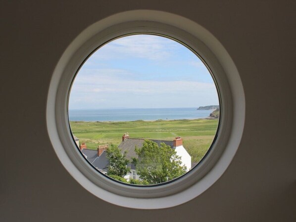 A round window with a view of a coastal landscape, including houses and a sea.