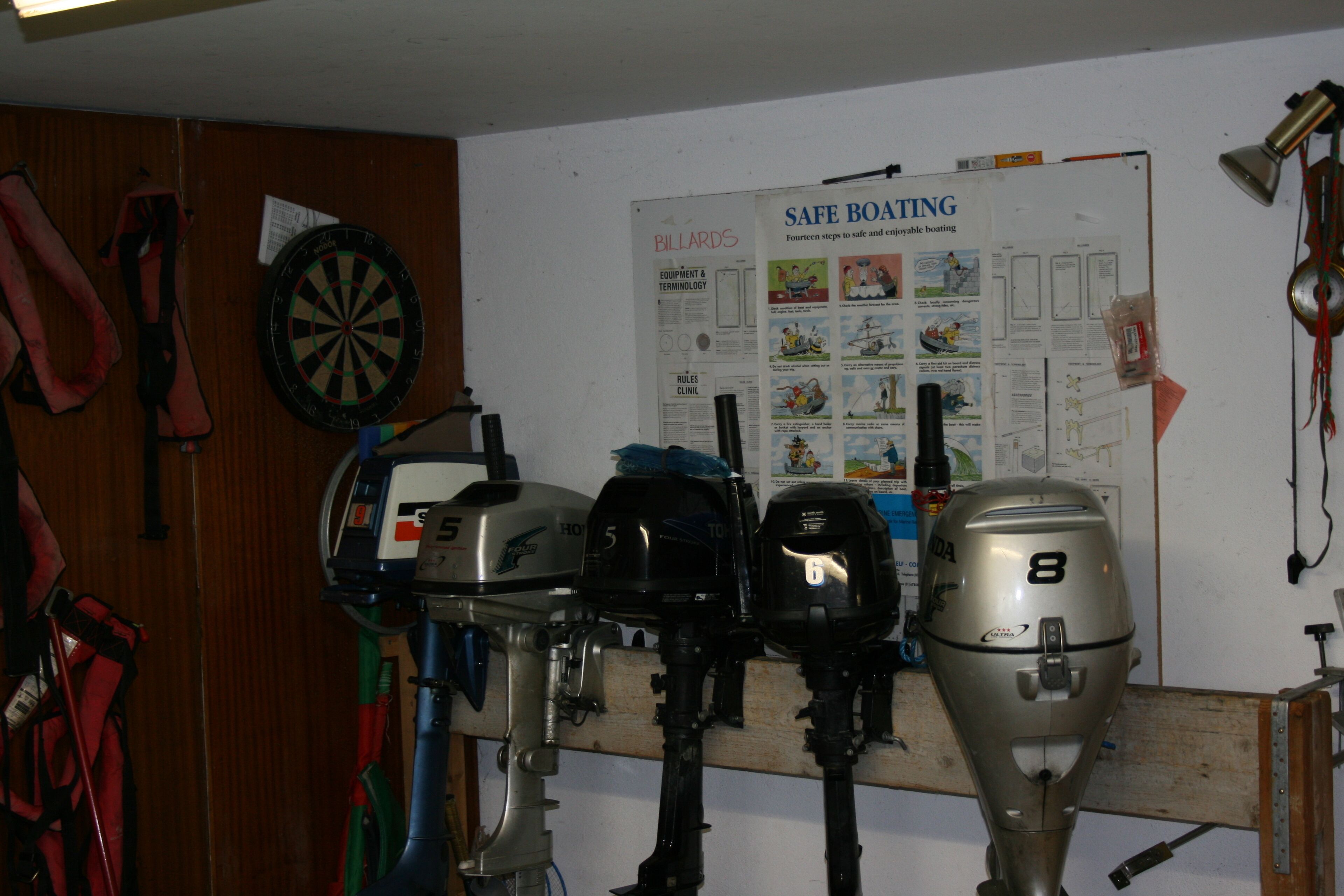 A room with four outboard motors lined up against a wall, a dartboard, and a poster titled "SAFE BOATING".