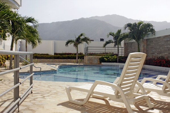 Zona de piscina con sillones de descanso, terraza de piedra y vistas a montañas al fondo.