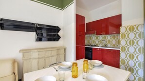 Un comedor con una mesa blanca dispuesta para cuatro personas, un radiador y una cocina con armarios rojos y salpicadero decorado.
