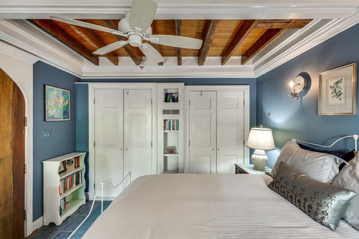 Une chambre à coucher comprenant un lit, un ventilateur de plafond, une table de chevet avec une lampe, une bibliothèque et une armoire.