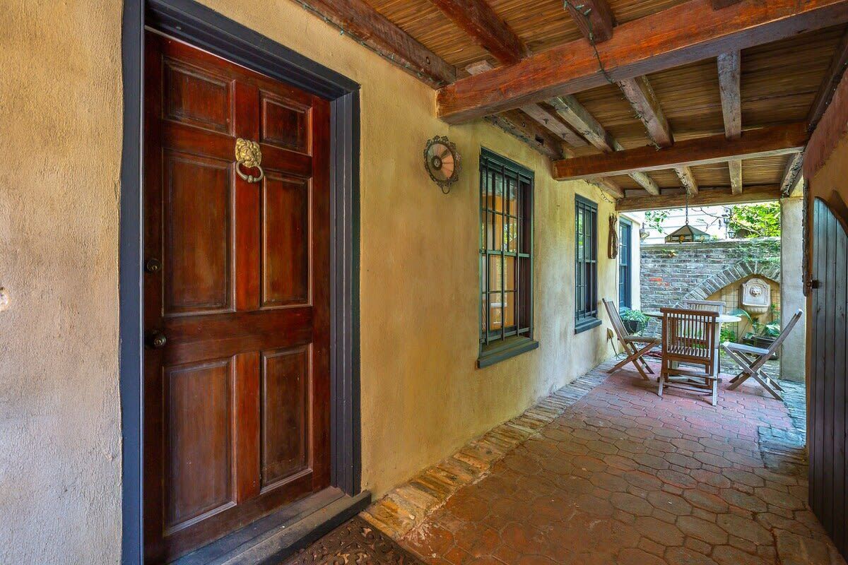 A corridor with a wooden door, a stone wall, and a small outdoor seating area with a table and chairs.