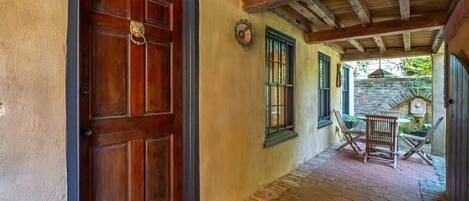 A corridor with a wooden door, a stone wall, and a small outdoor seating area with a table and chairs.
