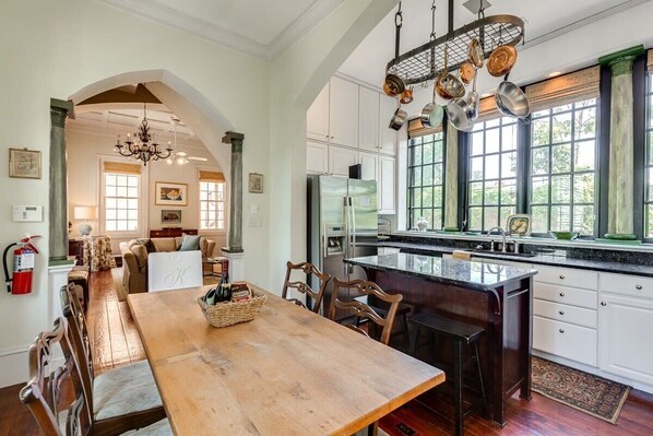 Une cuisine spacieuse dotée d’un grand îlot central, d’une table à manger en bois et offrant une vue sur l’extérieur grâce à de grandes fenêtres.