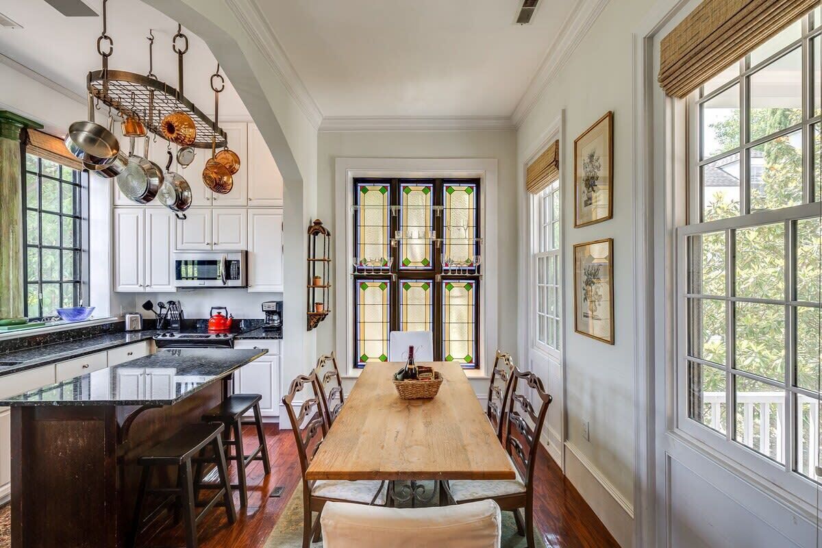 A kitchen with a central island, a dining table with chairs, and a large window with stained glass.