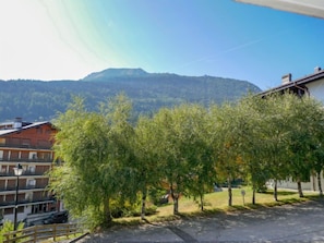 Uma área residencial com uma montanha ao fundo, uma rua com carros estacionados e uma fileira de árvores.