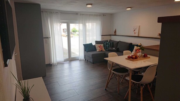 Un salon moderne avec un canapé, une table à manger et des chaises, ainsi qu’une grande fenêtre avec des rideaux.