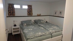 Une chambre à coucher comprenant un lit, deux tables de chevet, une fenêtre avec des rideaux et une étagère fixée au mur.