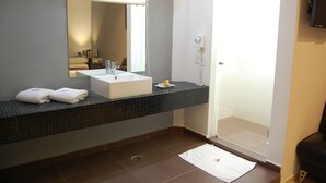 Un baño con lavamanos blanco, encimera con azulejos negros y puerta de ducha de cristal.