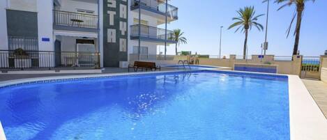 A swimming pool adjacent to a multi-story building with balconies.