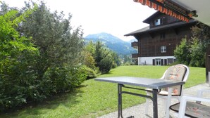 A patio with a table and chairs, a wooden house in the background, and a mountain view. - Diamant by Interhome (Zweisimmen)