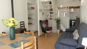 Ein Wohnzimmer mit blauem Sofa, einem Esstisch mit Stühlen, einer Treppe, die in eine Küche führt, und einem Bücherregal.