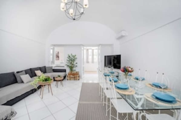A modern living room with a sofa, dining table, chairs, and a chandelier.