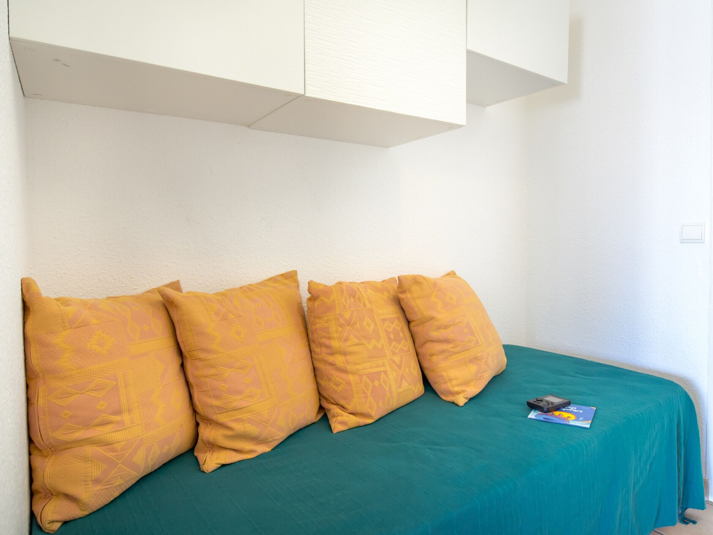A bed with a teal bedspread and three patterned pillows.