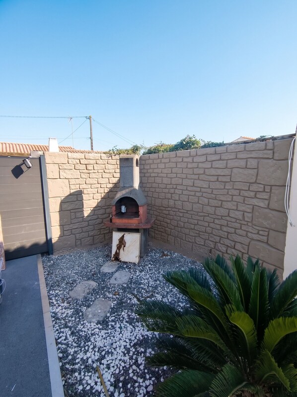 A backyard with a brick wall, a stone pathway, and a small outdoor oven.
